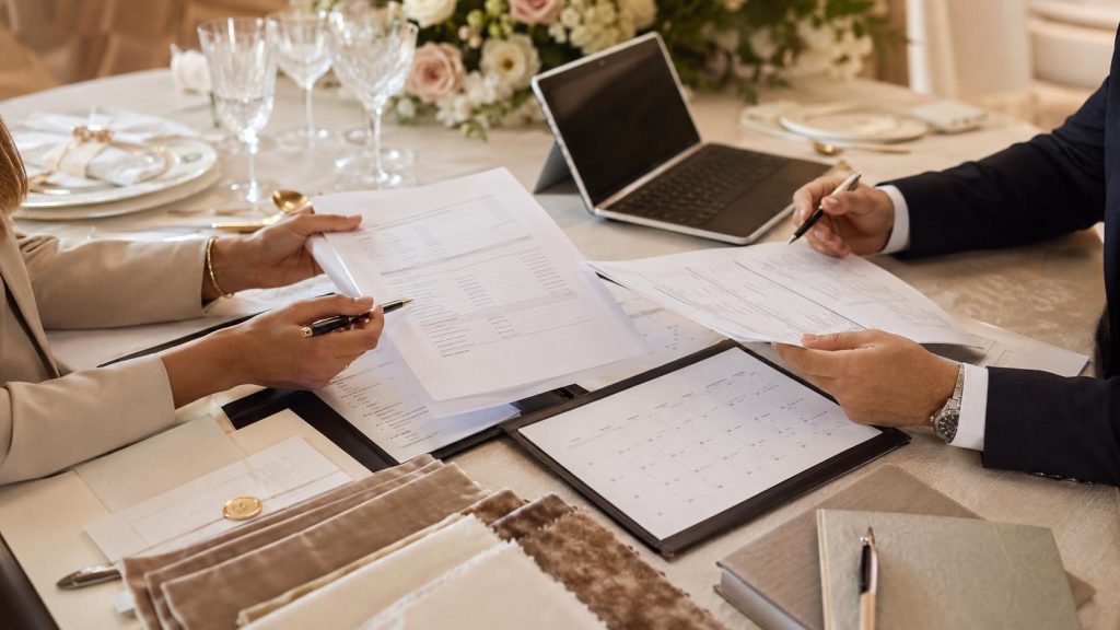 Professional catering booking review with contract documents, calendar, laptop, fabric swatches, and event tableware