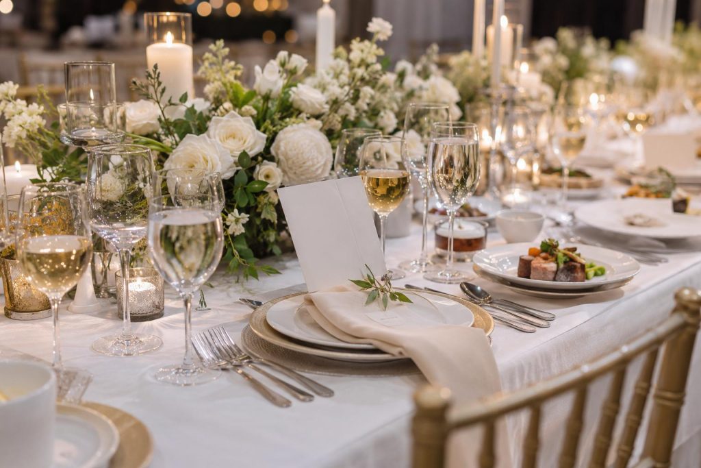 Close-up of wedding reception essentials with plated food, glassware, dinnerware, folded linens, flowers, and candles