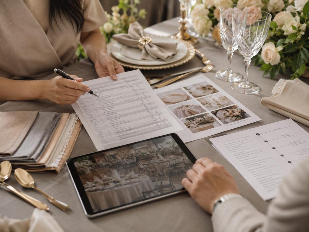 Hands reviewing a catering quotation, package checklist, tablet, linen swatches, tableware samples, and event documents