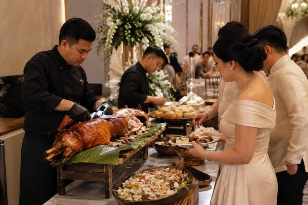 Chef carves lechon at a Filipino wedding buffet while guests are served traditional dishes