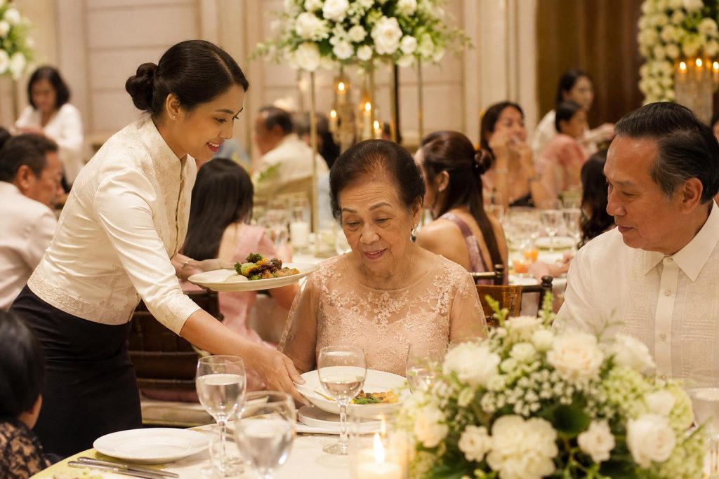 Banquet server assists elderly wedding guests with plated meals during a formal Filipino reception