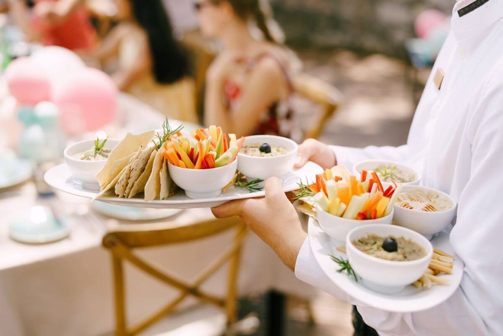 Servers carry plated comfort food appetizers for guests at a relaxed outdoor wedding reception