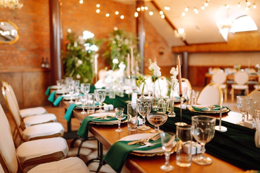 Styled wedding reception table with glassware, linens, candles, and formal place settings in a prepared venue