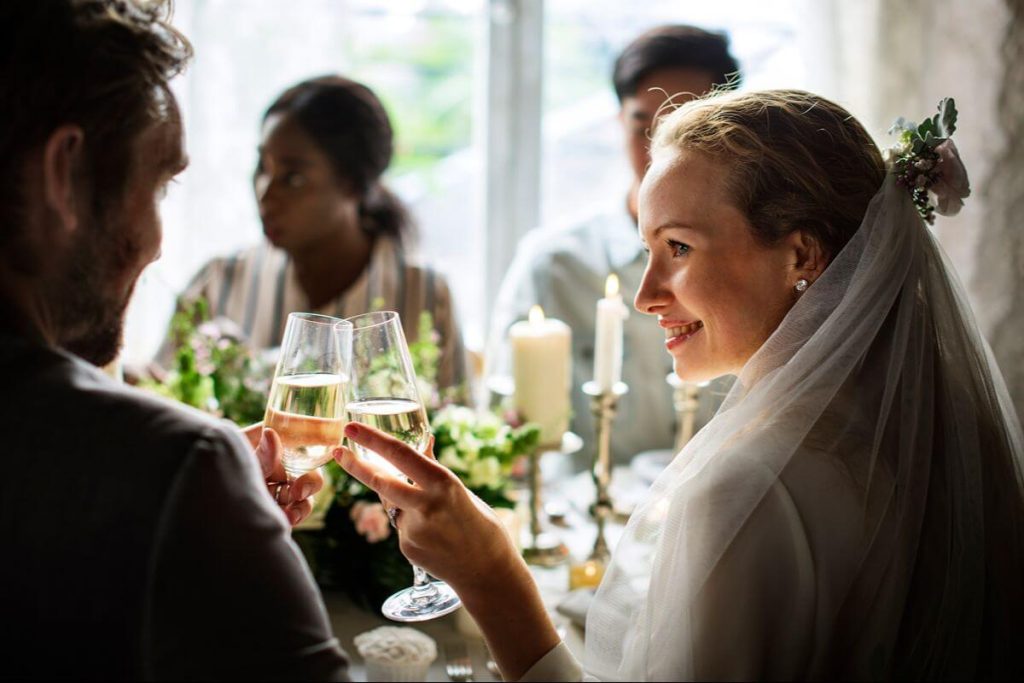 Bride and groom share a champagne toast during a relaxed wedding reception with guests in the background