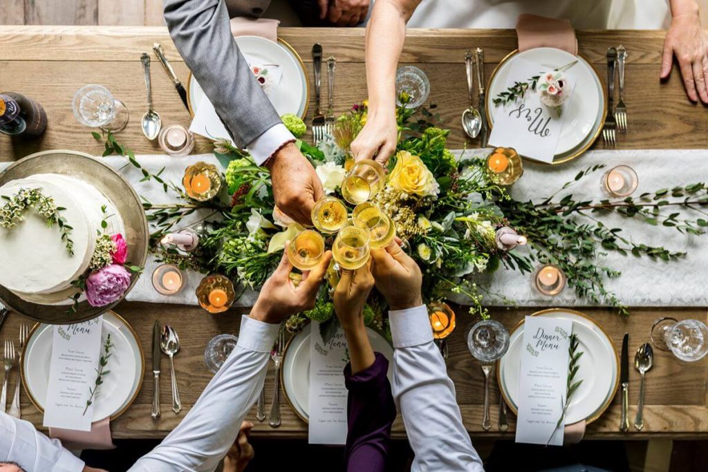 Wedding guests raise champagne glasses over a styled reception table with floral accents and formal place settings