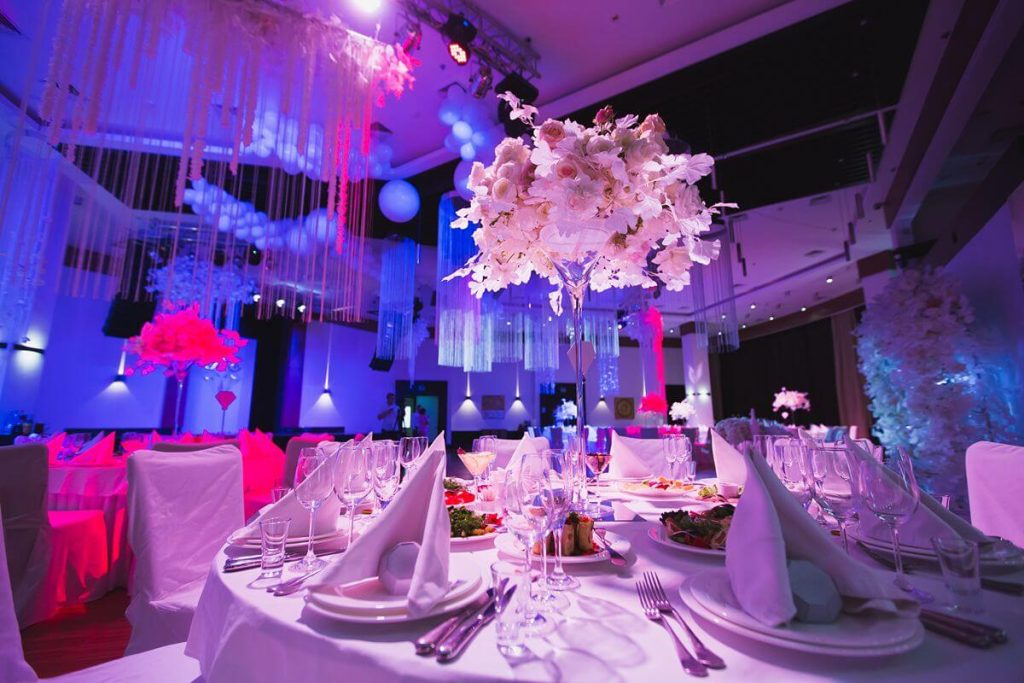 Elegant event table setup with floral centerpieces, plated meals, glassware, and colorful ambient lighting