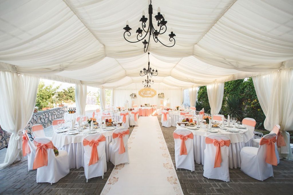 Elegant wedding reception venue with decorated tables, chairs, draped ceiling, and coordinated event setup
