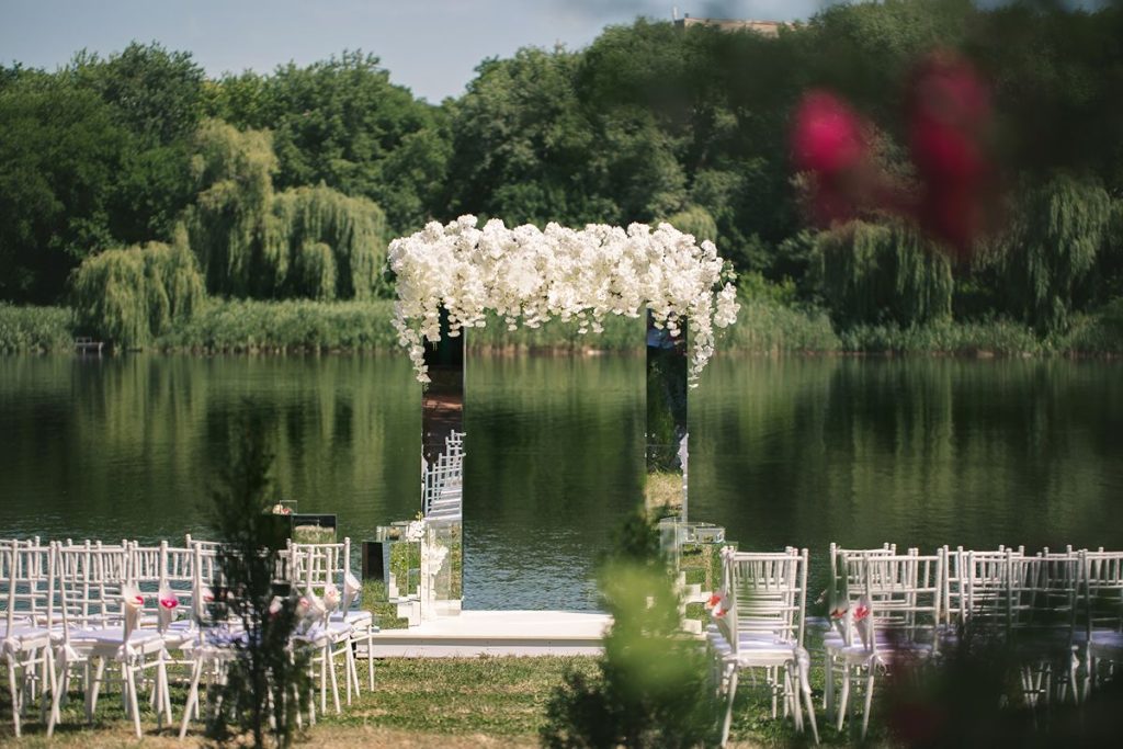 Lakeside wedding ceremony setup with white chairs, floral arch, and scenic water backdrop