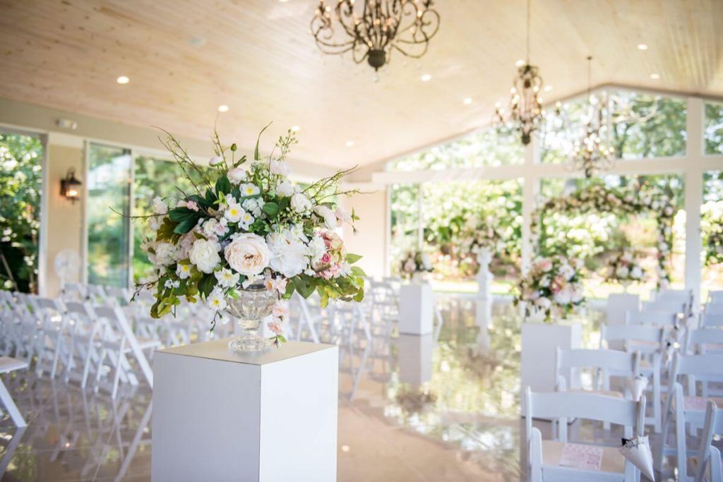 Styled wedding ceremony setup with white chairs, floral arrangements, and elegant indoor décor